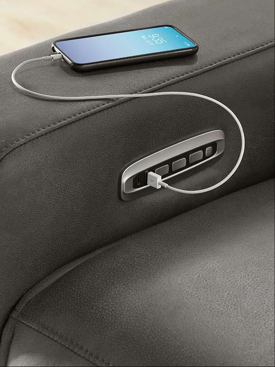 A smartphone charging on a dark gray leather recliner.
