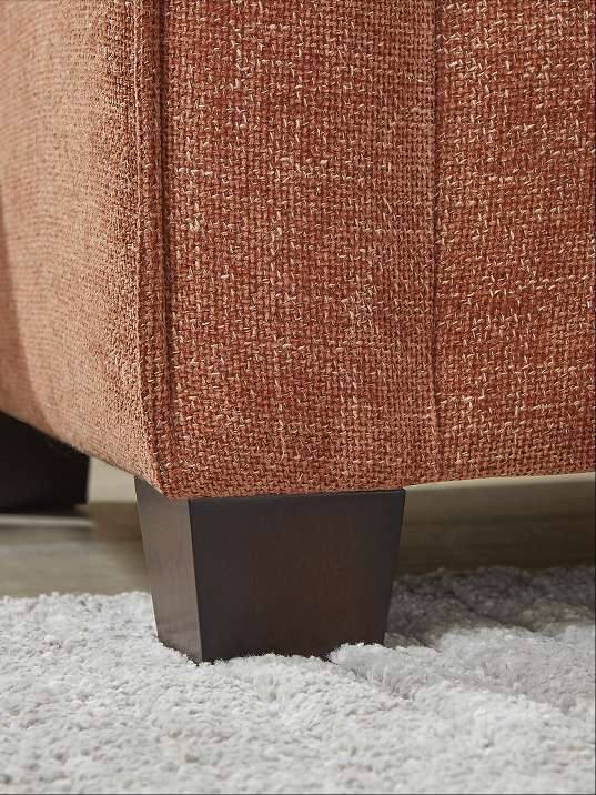 Close-up of a brown upholstered couch with dark wooden legs on a white rug.
