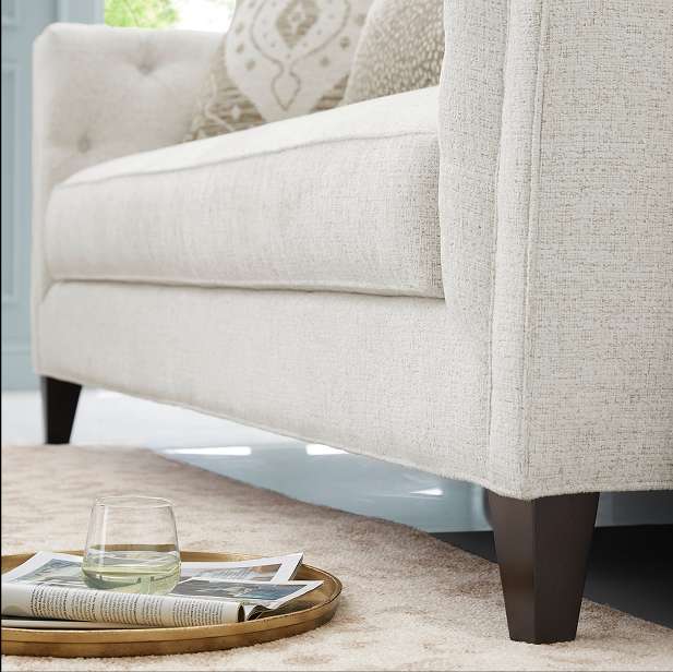 Cream-colored upholstered armchair with dark wooden legs, a tray with a glass and newspaper on the rug.
