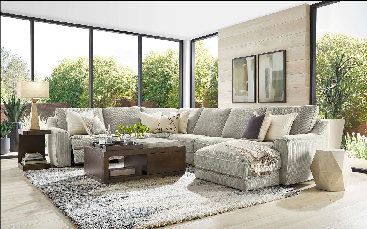 A gray sectional sofa with decorative pillows and a coffee table on a patterned rug.
