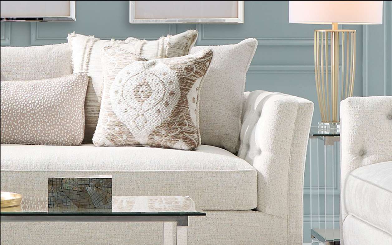 A cream-colored sofa with decorative pillows and a side table with a lamp.
