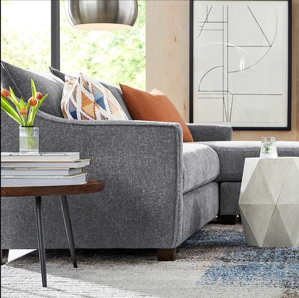 Gray sectional sofa with throw pillows, a side table, and a rug.
