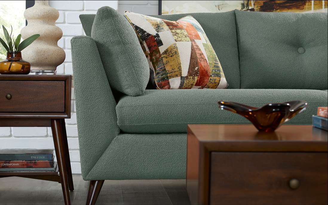 Green sofa with a patterned pillow, a side table, and a coffee table.
