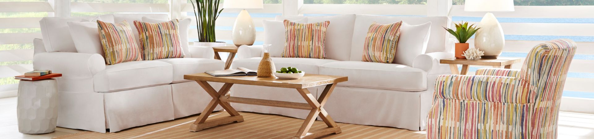 White sofas with colorful striped pillows and a matching armchair, with a wooden coffee table and side tables.
