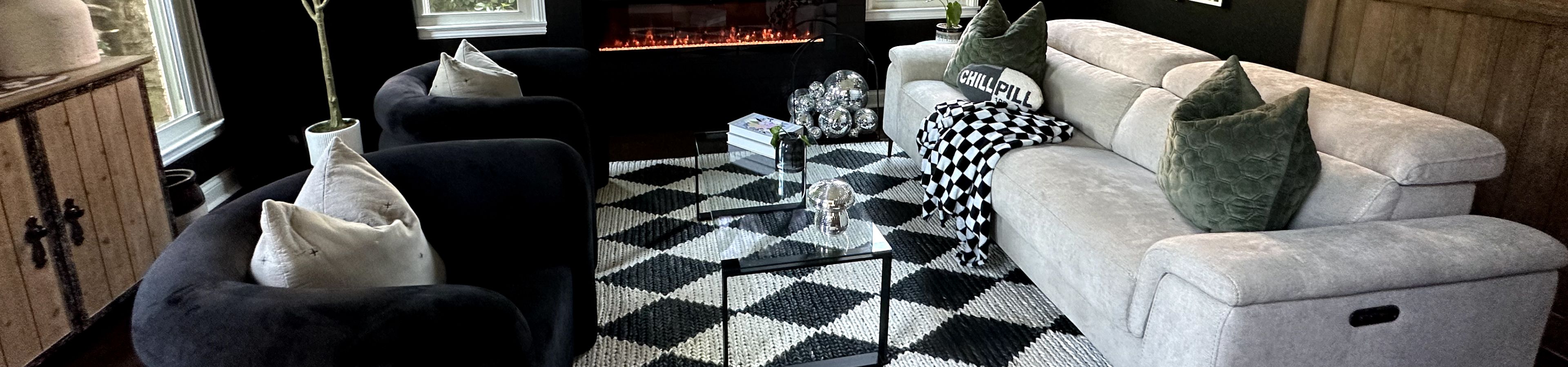 A living room with black walls, black chairs, a light gray sofa, and a black and white rug.
