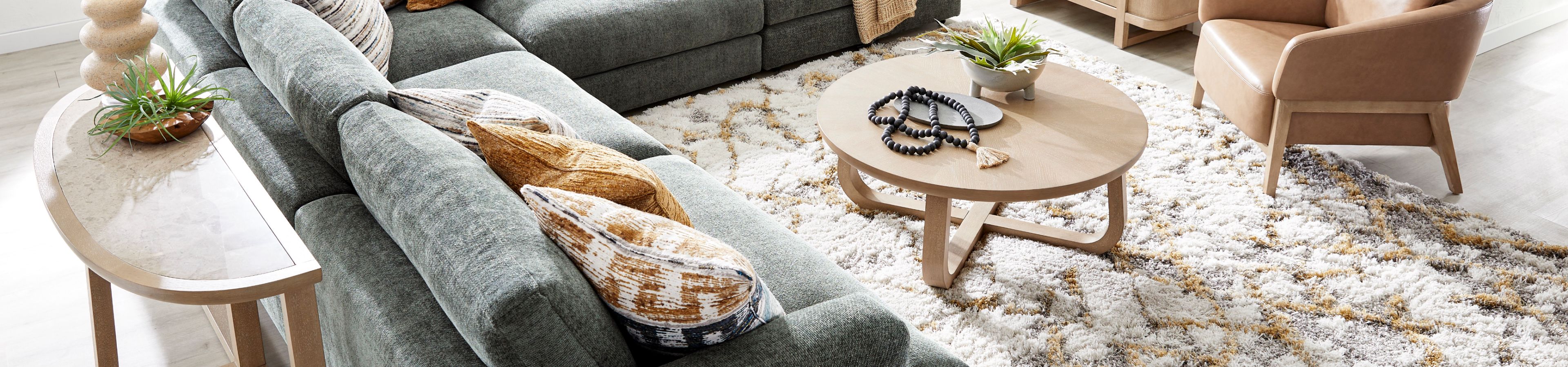 A sectional sofa with decorative pillows, a round coffee table, and a patterned rug.
