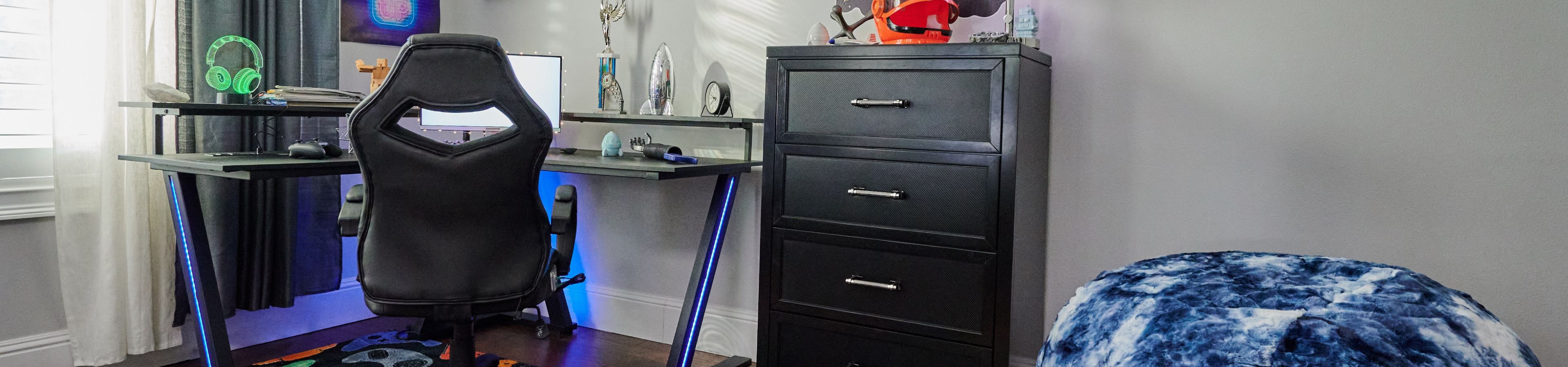 A gaming desk with a black chair, a black dresser, and a blue beanbag.
