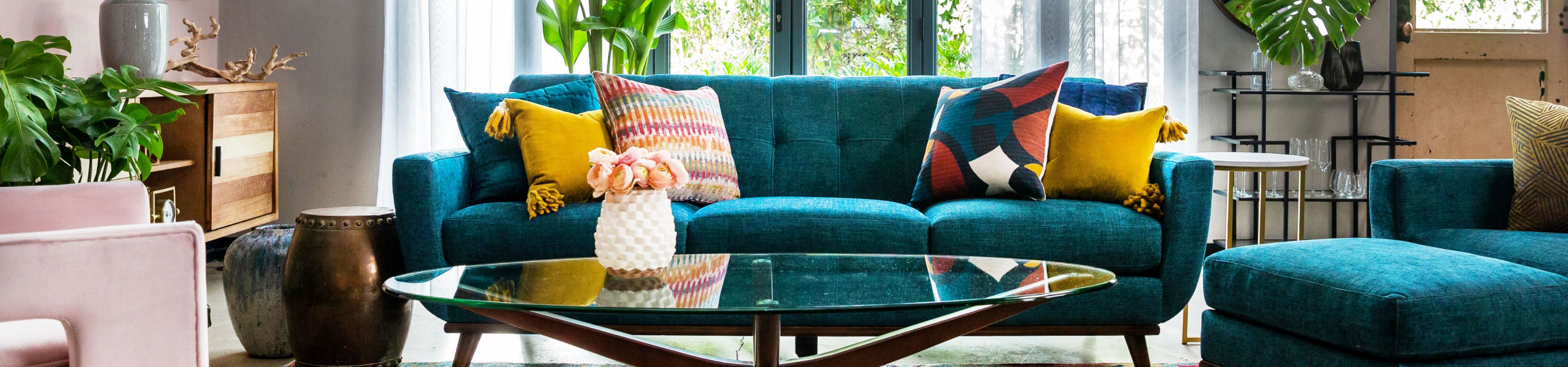 Teal sofa with colorful pillows and a glass coffee table.

