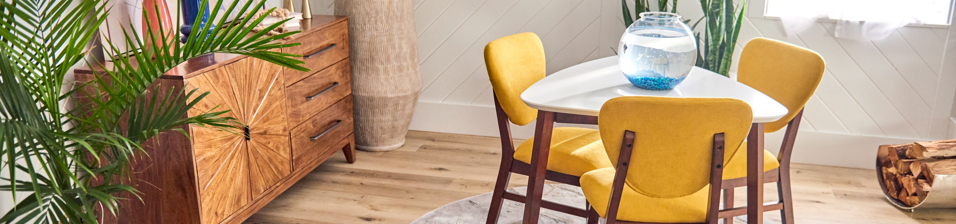 A dining table with yellow chairs, a fishbowl, and a wooden cabinet.
