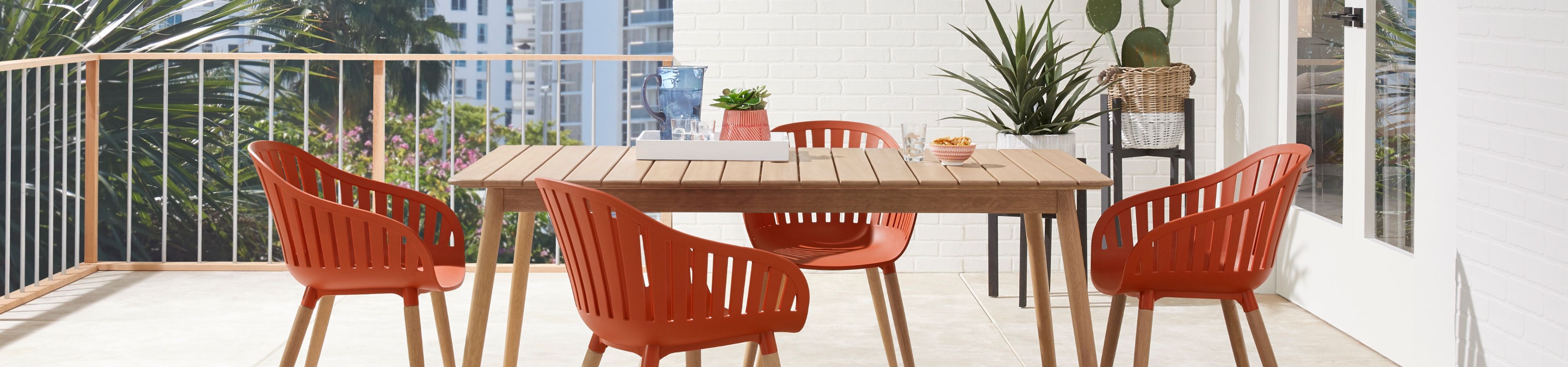 Outdoor dining set with orange chairs and a wooden table on a balcony.
