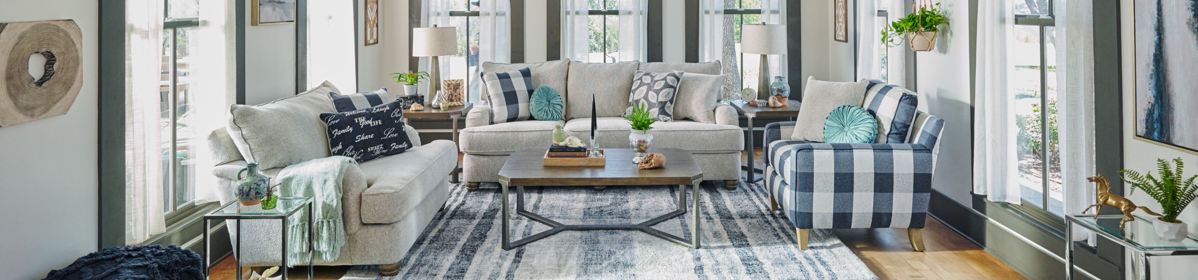 Living room with light-colored sofas, patterned pillows, and a checkered armchair. A rug and coffee table are in the center.