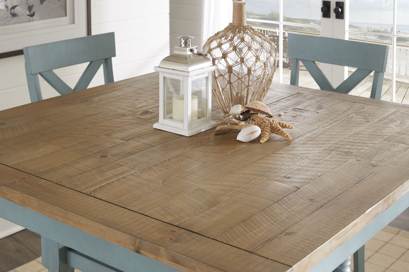 Wooden dining table with blue legs and chairs, decorated with a lantern, shells, and a starfish.
