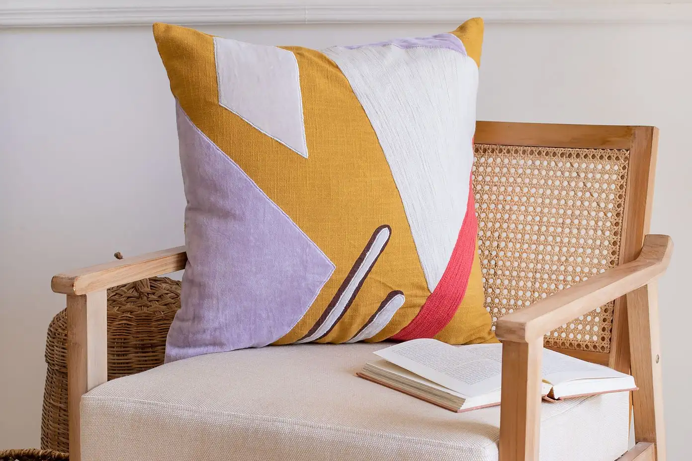 A decorative pillow with an abstract design on a wooden chair with a book.
