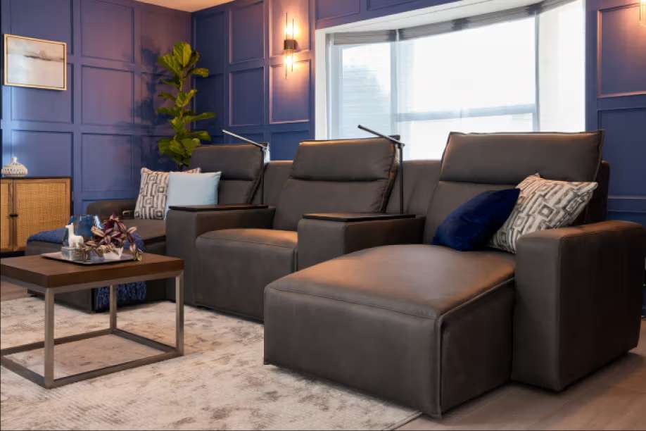 A dark gray leather sectional sofa with a chaise lounge in a blue-walled room.
