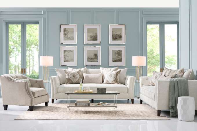 Living room with light-colored furniture, artwork, and a glass coffee table.
