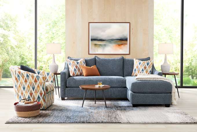 A living room with a blue sectional sofa, patterned armchair, and a rug.

