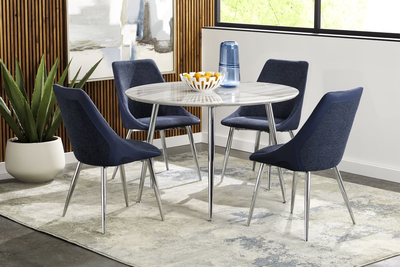 A round dining table with four blue chairs on a patterned rug.

