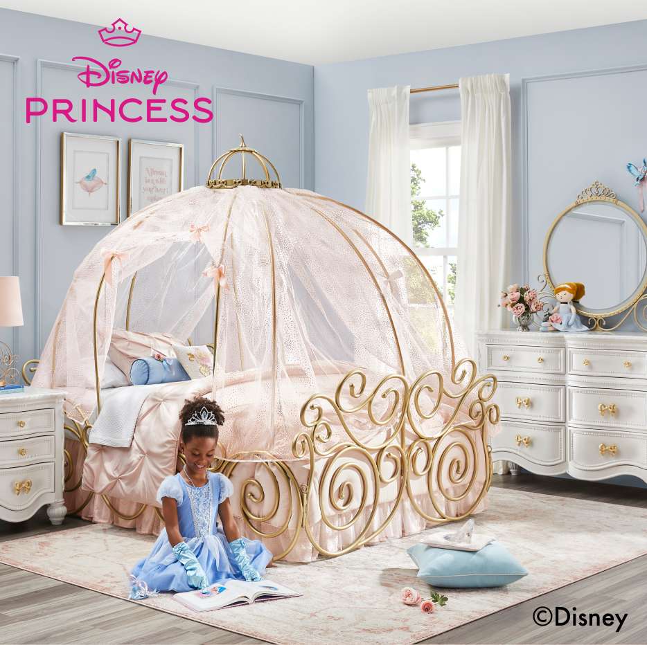 Disney Princess. A girl in a Cinderella dress sits on the floor reading a book in front of a princess bed.