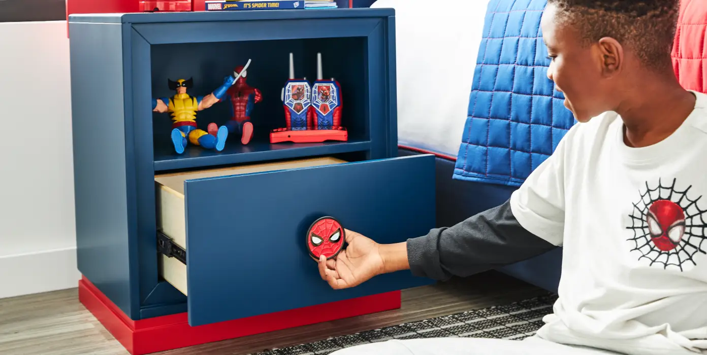 A young boy opening a blue Spider-Man themed nightstand drawer with a Spider-Man mask knob.