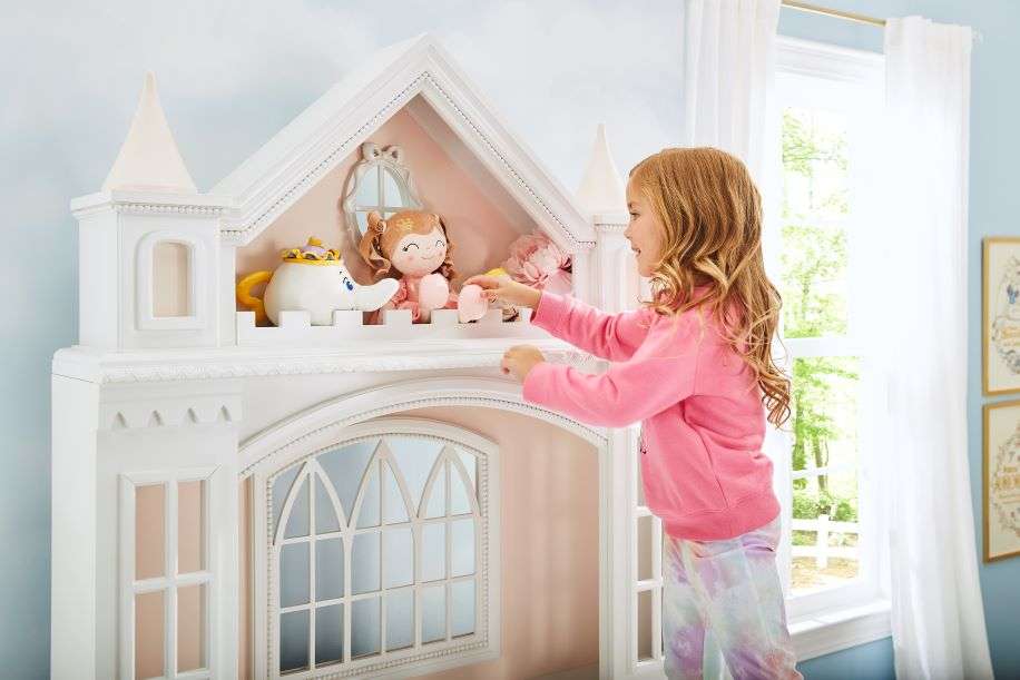 A young girl playing with a white dollhouse.