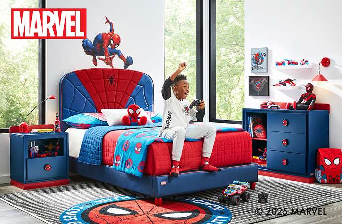 MARVEL. A boy plays a video game on a Spider-Man themed bed.
