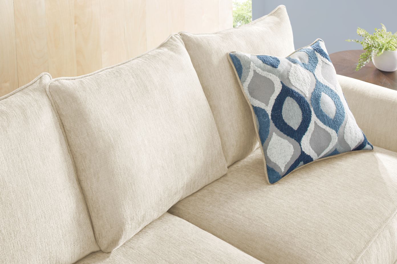 Cream-colored sofa with a patterned blue and gray pillow.

