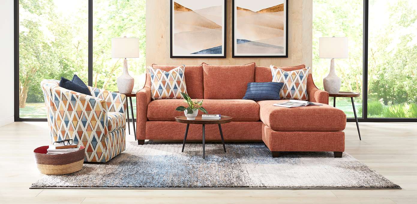 Living room with a rust-colored sectional sofa, patterned armchair, and a patterned rug.
