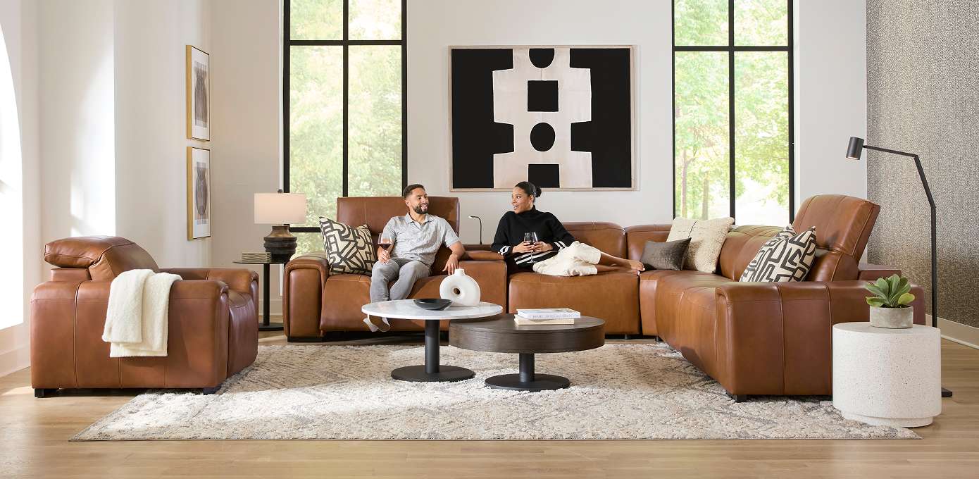 A living room with brown leather furniture, a rug, and two people.
