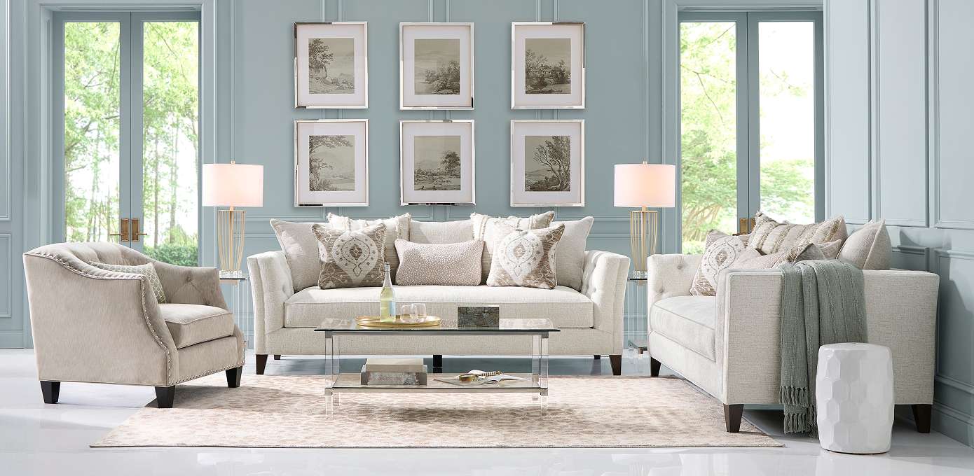 Living room with light-colored furniture, a glass coffee table, and landscape art on the wall.
