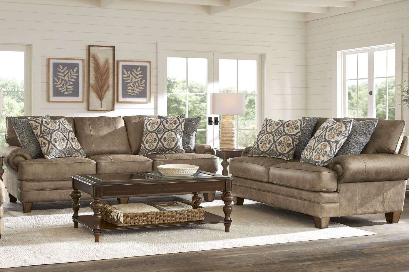 Brown leather sofa and loveseat with patterned pillows, coffee table, and artwork.