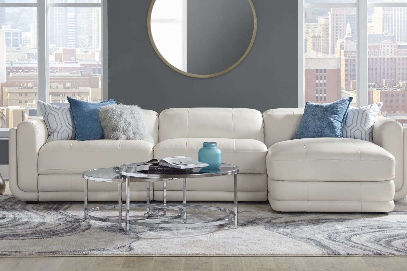 White sectional sofa with blue pillows, a round coffee table, and a rug.

