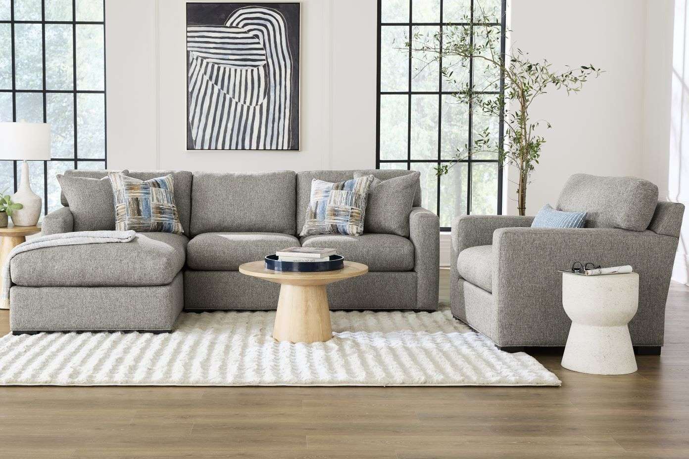 Gray sectional sofa with patterned pillows, a round wooden coffee table, and a white rug.
