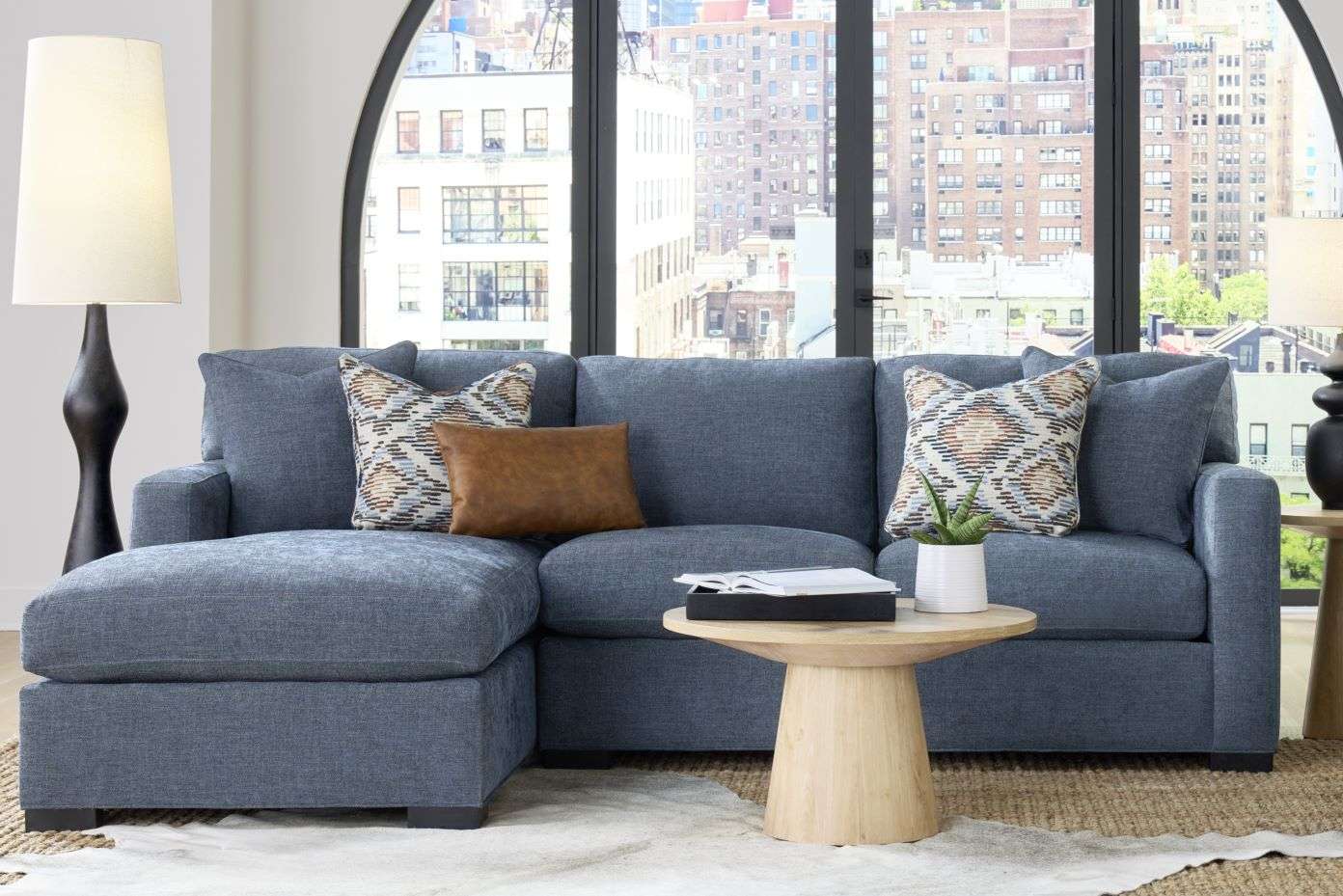 Blue sectional sofa with patterned pillows and a small wooden side table.
