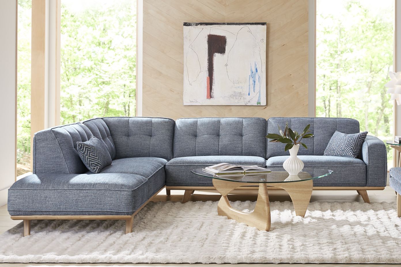 Blue sectional sofa with a glass coffee table and a white rug.
