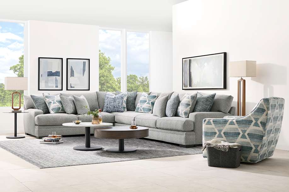 Gray sectional sofa with patterned pillows, two round coffee tables, and a patterned accent chair.
