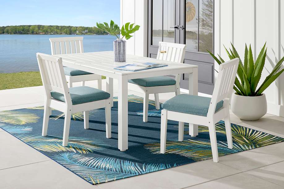 White outdoor dining set with blue cushions on a tropical rug.
