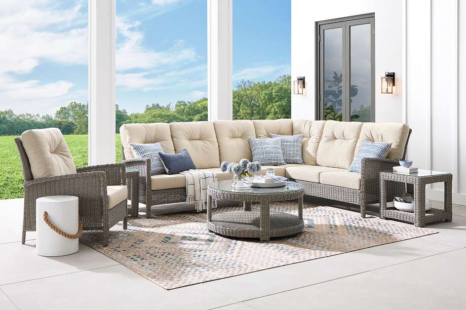 Outdoor sectional sofa with matching side tables and a round coffee table on a patterned rug.

