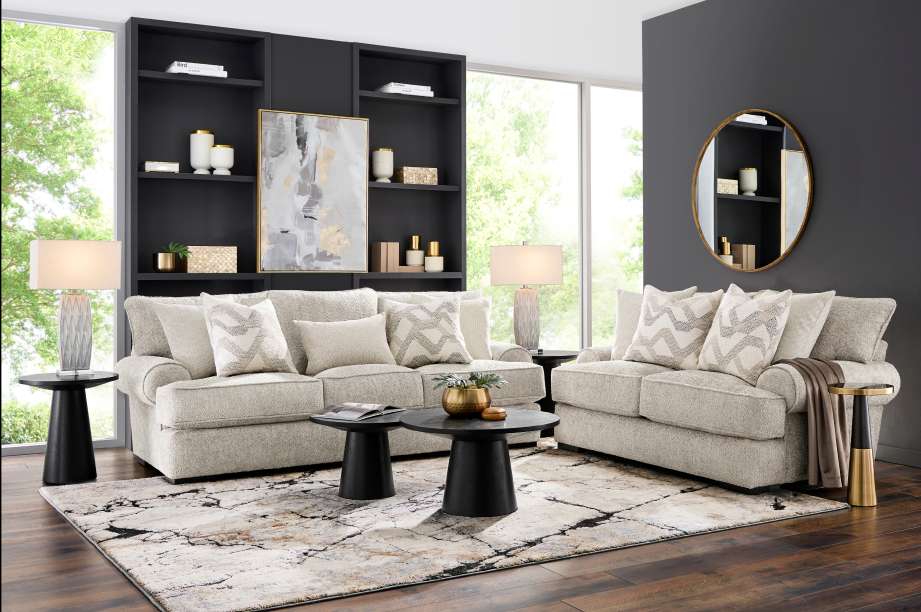 Living room with light-colored sofas, patterned rug, black tables, and a round mirror.
