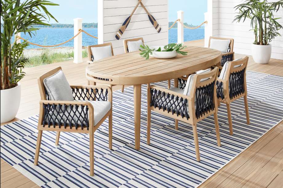 Outdoor dining set with a wooden oval table and woven chairs on a striped rug.
