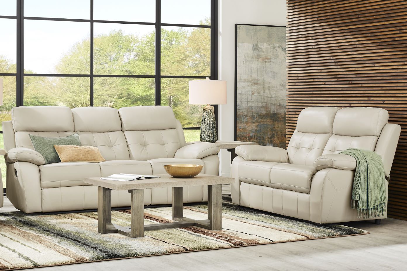 Cream-colored leather sofa and recliner with a coffee table and rug in front of a large window.
