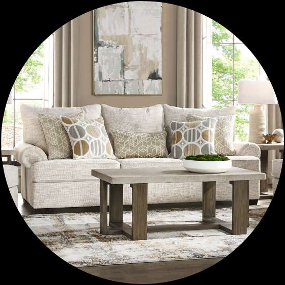 Living room with a beige sofa, patterned pillows, a concrete coffee table, and a rug.
