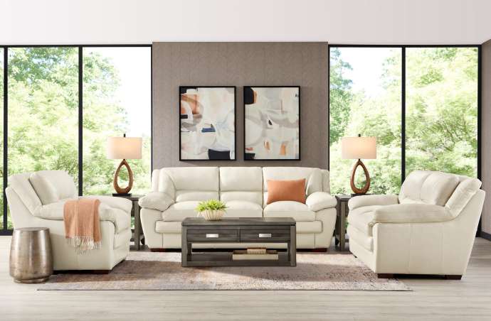 Living room with white leather sofa, two armchairs, coffee table, and artwork.
