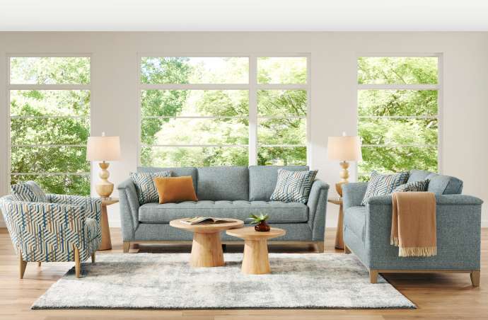 Living room with blue sofas, patterned armchair, wooden tables, and a rug.
