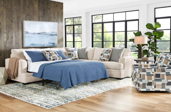 Beige sectional sofa with a pull-out bed, blue bedding, and patterned pillows.

