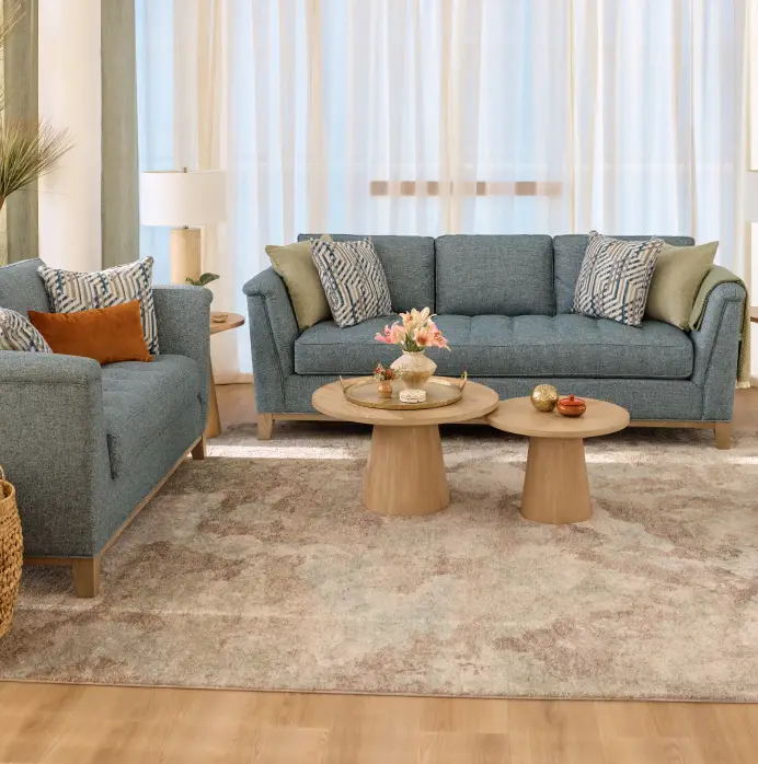 A blue fabric sofa and matching armchair with patterned and solid throw pillows, arranged around two round wooden coffee tables.