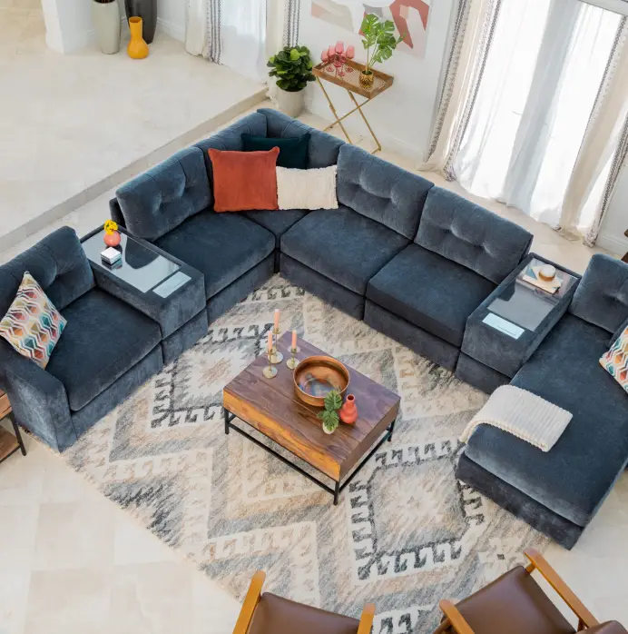 A large, dark blue sectional sofa with built-in side tables, arranged around a wooden coffee table on a patterned rug.