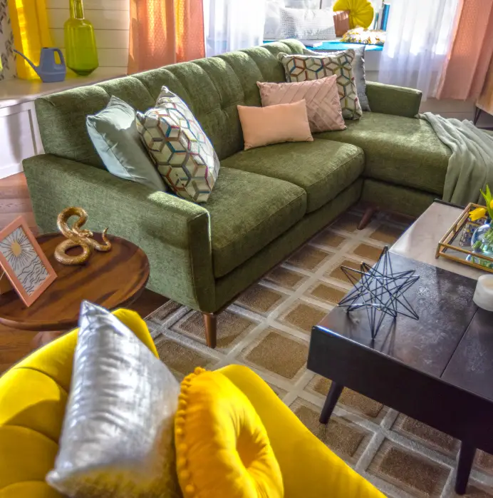 A green sectional sofa with patterned and solid pillows, a yellow armchair, and a coffee table in a bright living room.