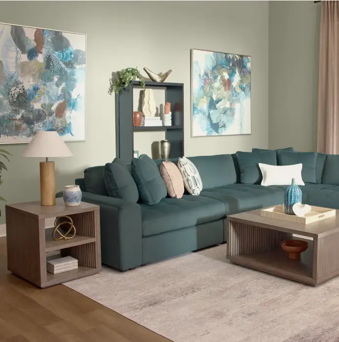A teal sectional sofa with decorative pillows, a wooden side table with a lamp, and a matching coffee table on a rug.