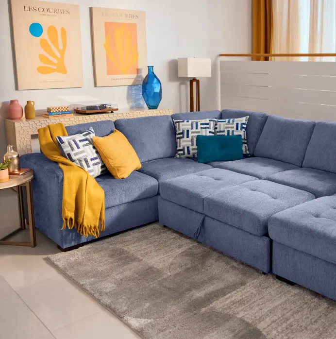 A blue sectional sofa with yellow throw blankets and patterned pillows in a modern living room.
