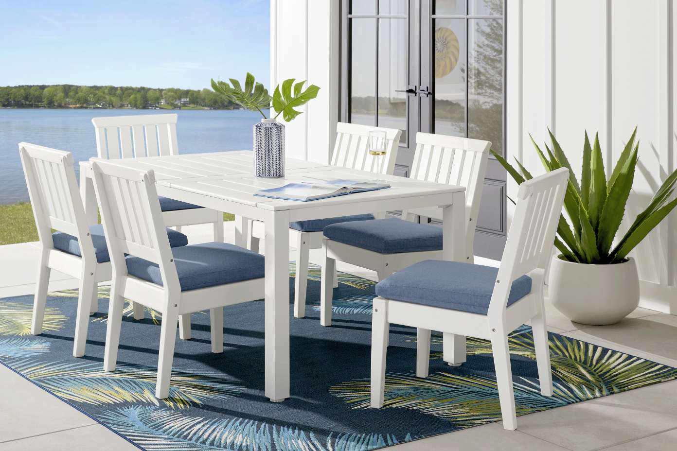 White outdoor dining set with blue cushions on a blue patterned rug.
